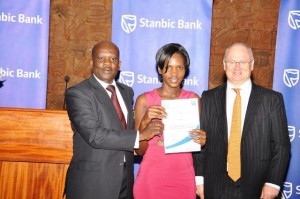 Stanbic Head of Personal and Business Banking Kevin Wingfield (R) and Enterprise Uganda Executive Director Charles Ocici hand over a certificate to Mary Asiimwe, a jewelry designer who was one of the Top 10 SME participants who graduated from the one year Stanbic Business Mentoring Programme 